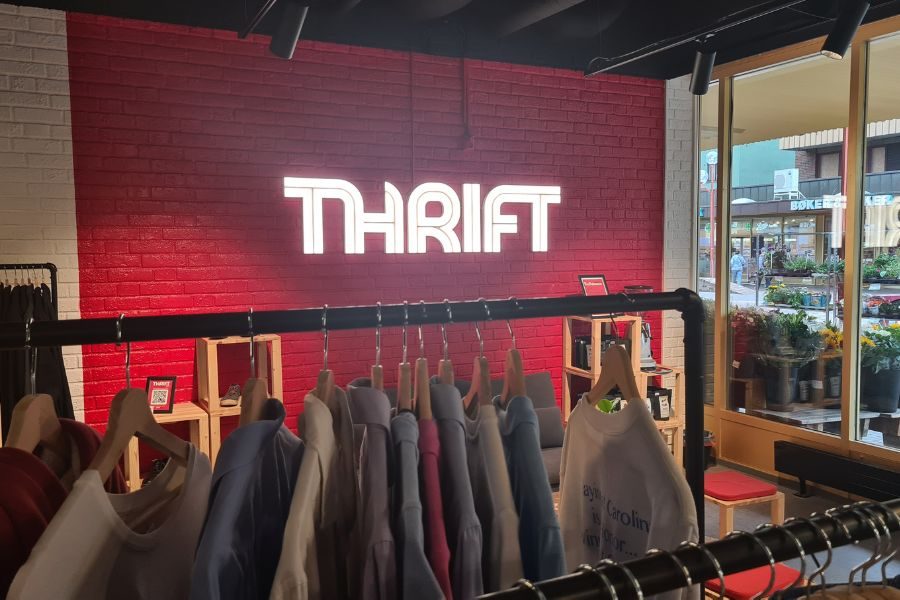 Klær på stativ og detaljvegg med lysende THRIFT hos Thrift Tøyen