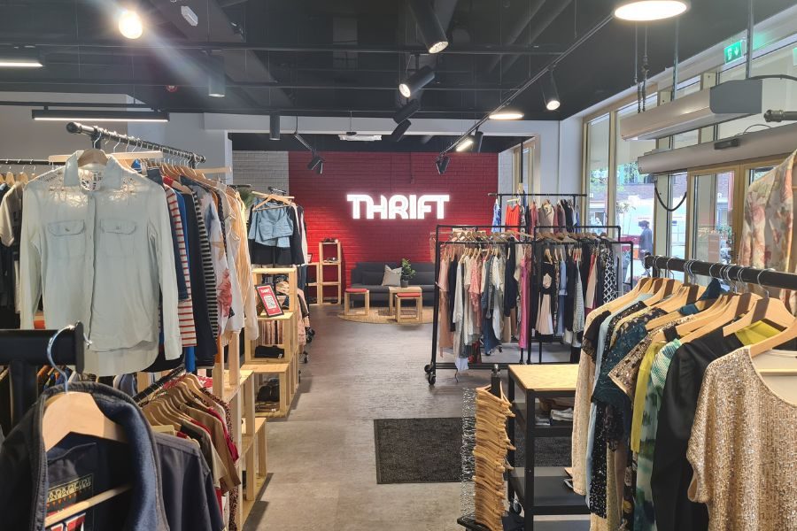 Store lokaler med mange stativ med klær og detaljvegg med lysende THRIFT hos Thrift Tøyen